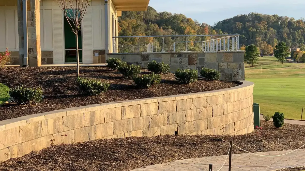 Curved stone retaining wall with lush green shrubs and mulch, enhancing a landscaped outdoor space near a modern building in Gibsonia, PA.