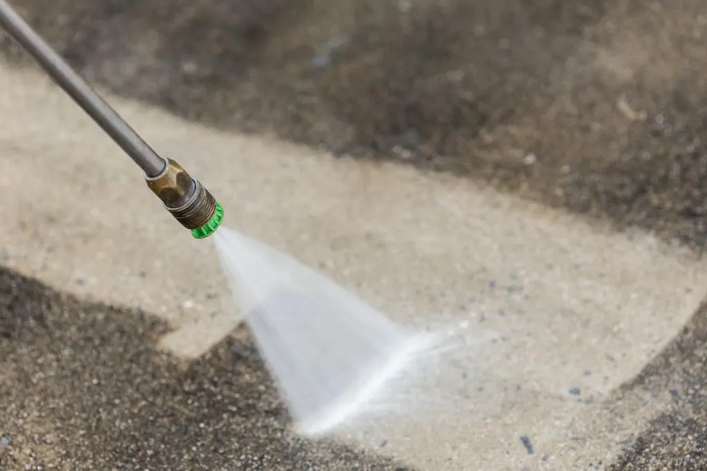 Pressure washer nozzle spraying water on a concrete surface, illustrating professional pressure washing services for outdoor cleaning.